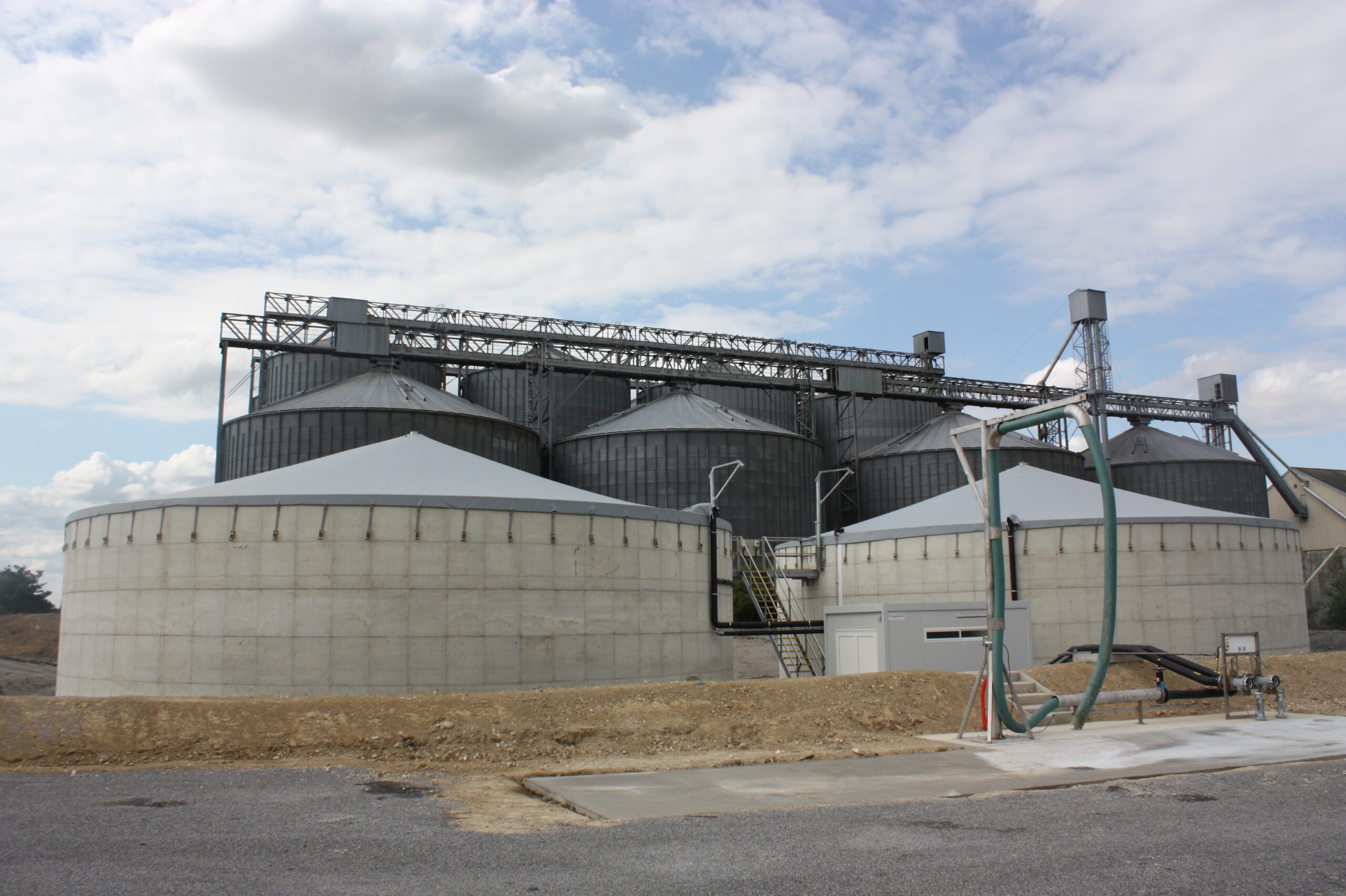 Twee betonnen opslagtanks met spankap naast stalen silo's op een industrieterrein
