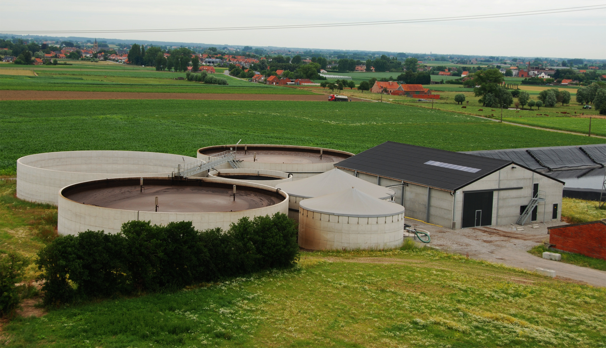 Ronde betonnen opslagtanks op een bedrijf met woningen en een dorpskern op de achtergrond