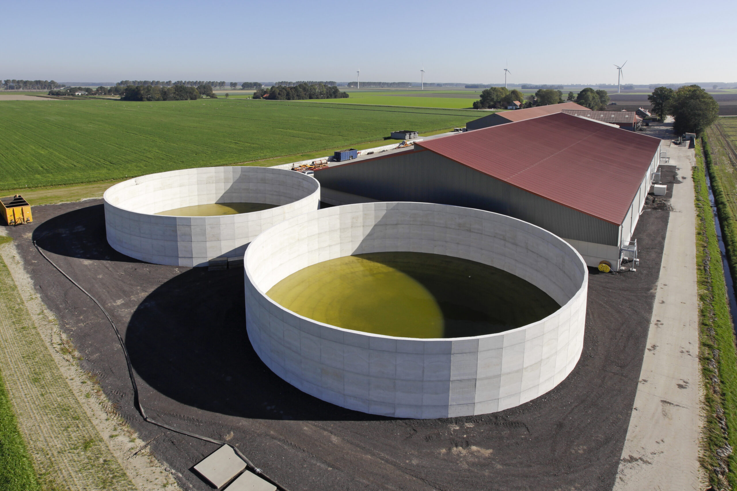 Twee ronde betonnen opslagtanks naast een stal op een landbouwbedrijf