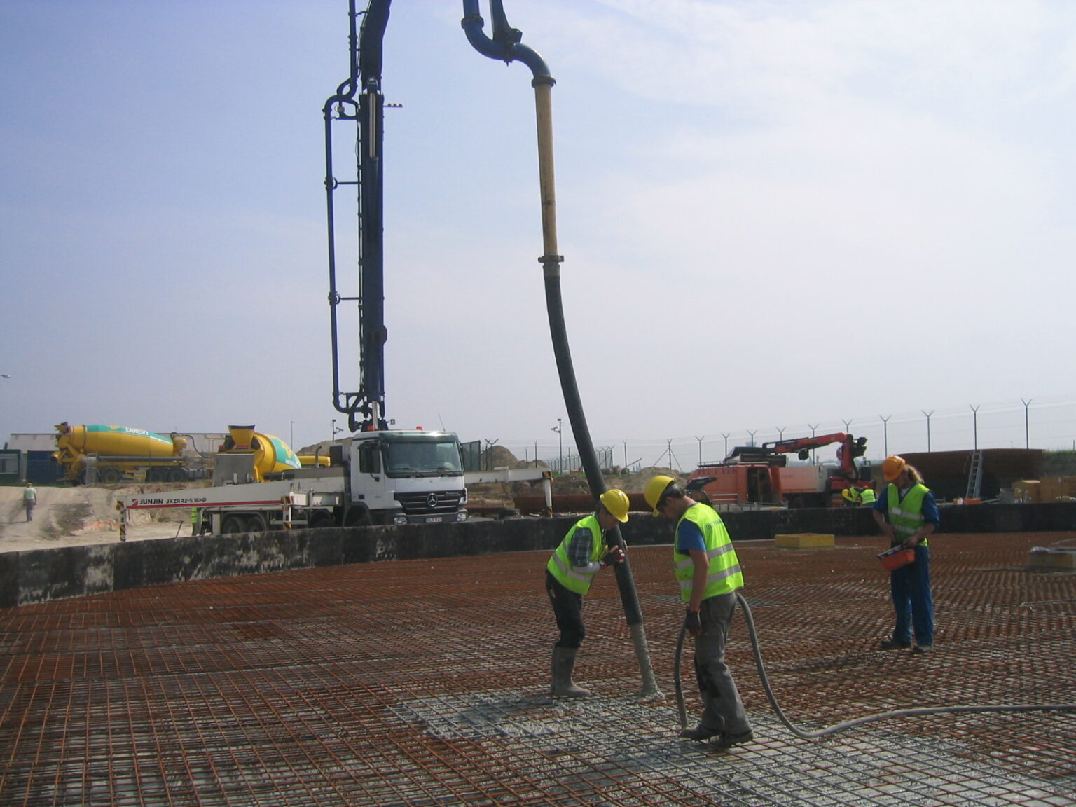 Betonvloer van een opslagtank die met een betonpomp wordt gestort over een vlechtwerk van wapening, met twee werklieden aan de slang